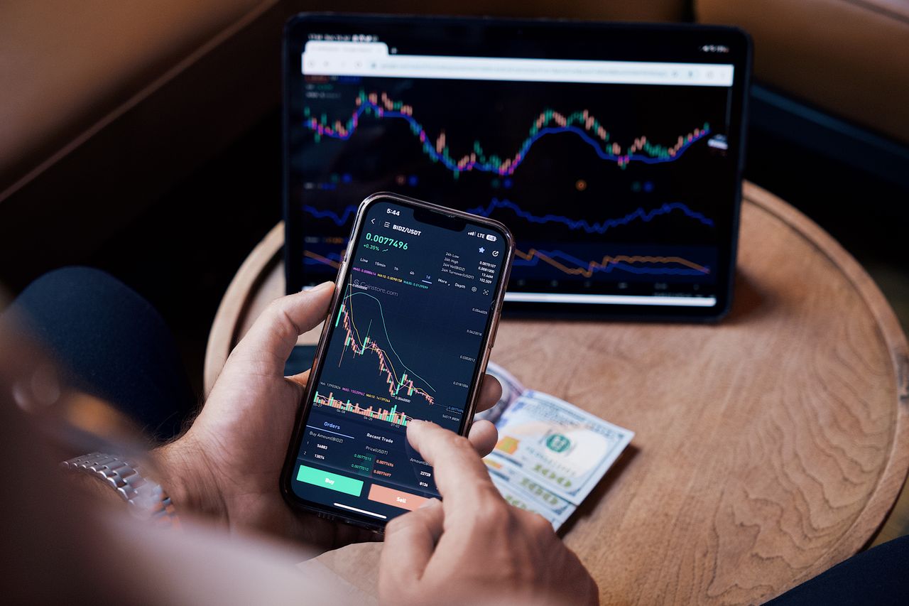 A detailed view of an individual engaging in stock trading via a smartphone and a tablet.